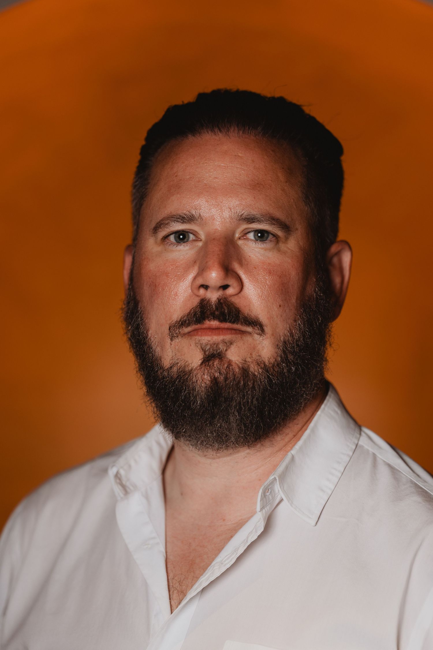 Professional headshot of a bearded man in white shirt with orange studio lighting.