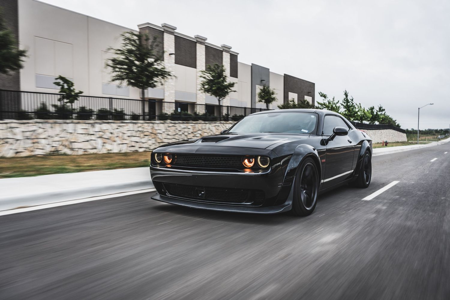 Black Dodge Challenger with custom widebody kit photographed in motion on city street.