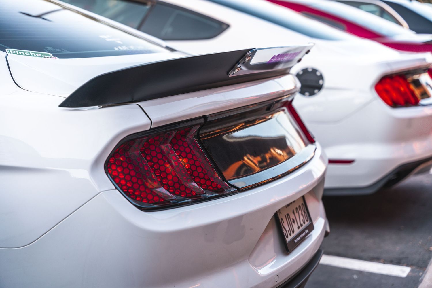 Close up of white Ford Mustang tail light and rear spoiler in parking lot.