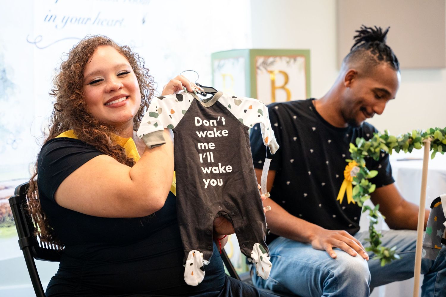 A guest holds up a small dark onesie at a baby shower celebration.