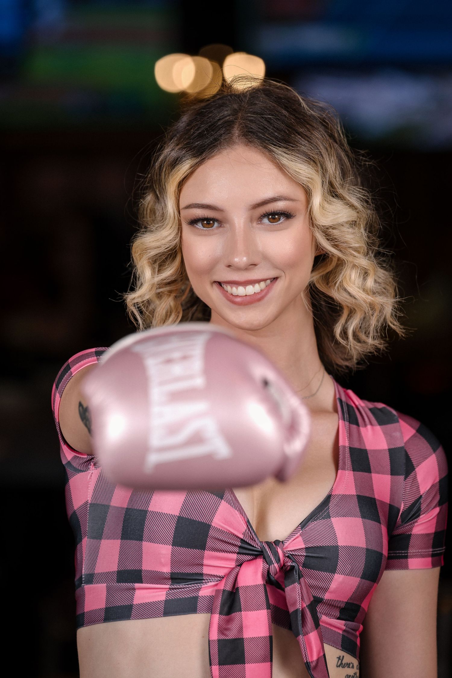 Model shows pink boxing glove while wearing matching pink plaid crop top.