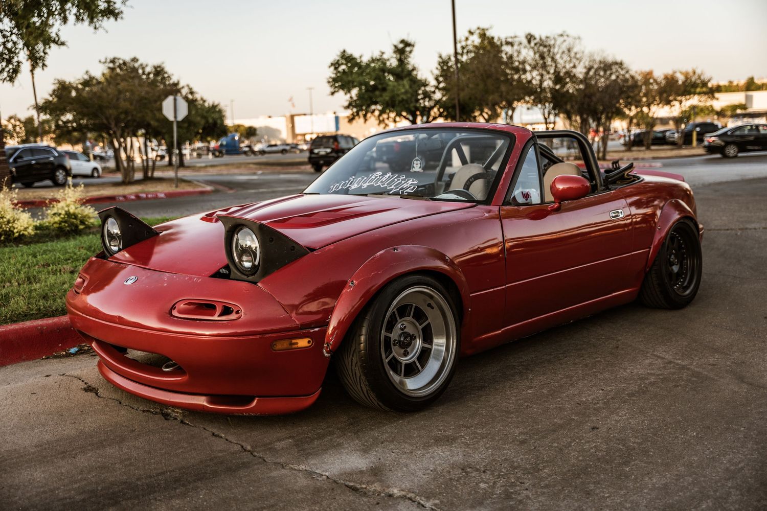 Modified red Mazda Miata with wide body kit and aftermarket wheels.