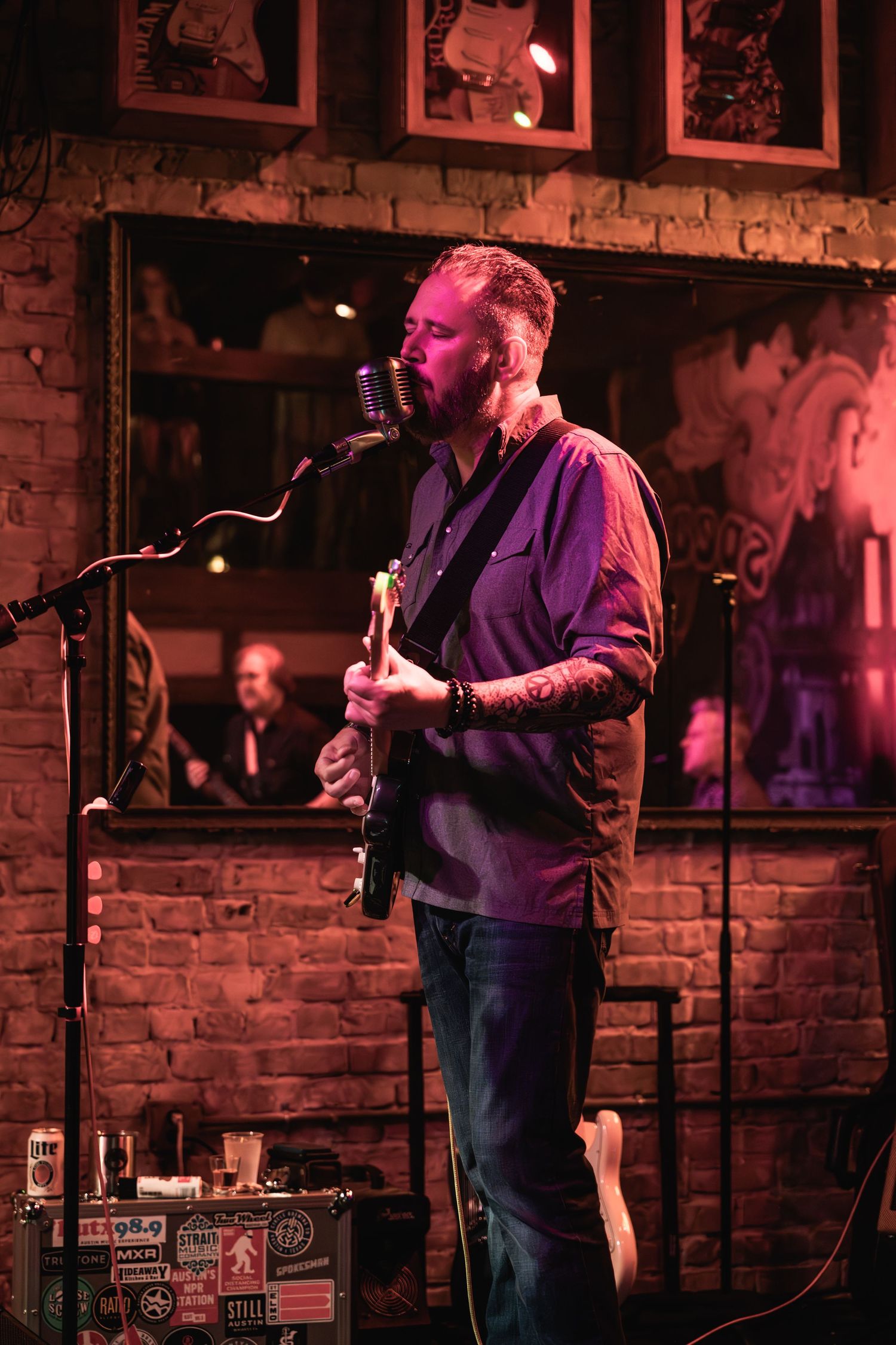 Musician performing with guitar against brick wall backdrop in dim lighting.