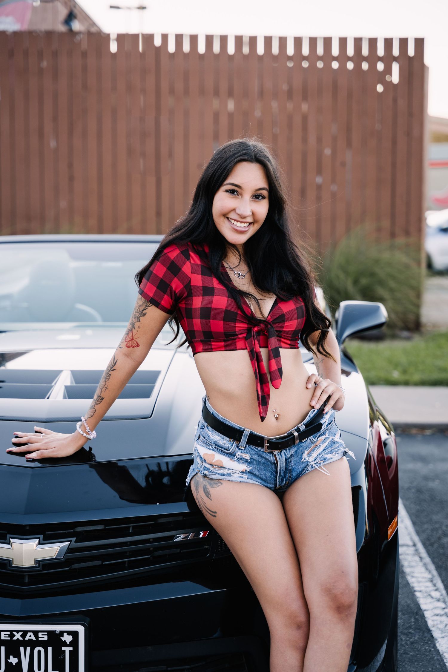 Brand ambassador posing next to a black Chevrolet at a car show.