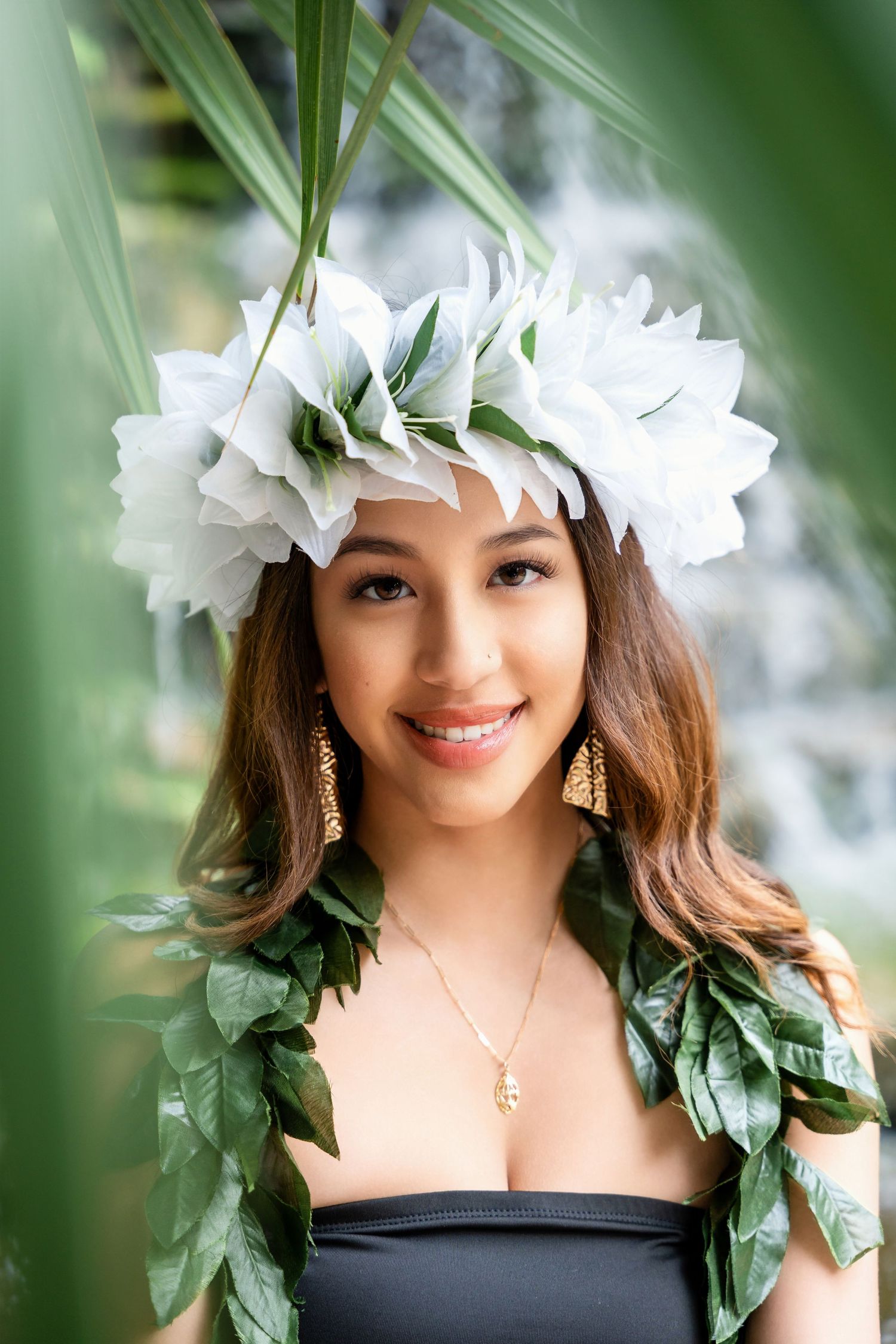 Tropical graduation photo with white flower crown and green leaf lei against blurred background.
