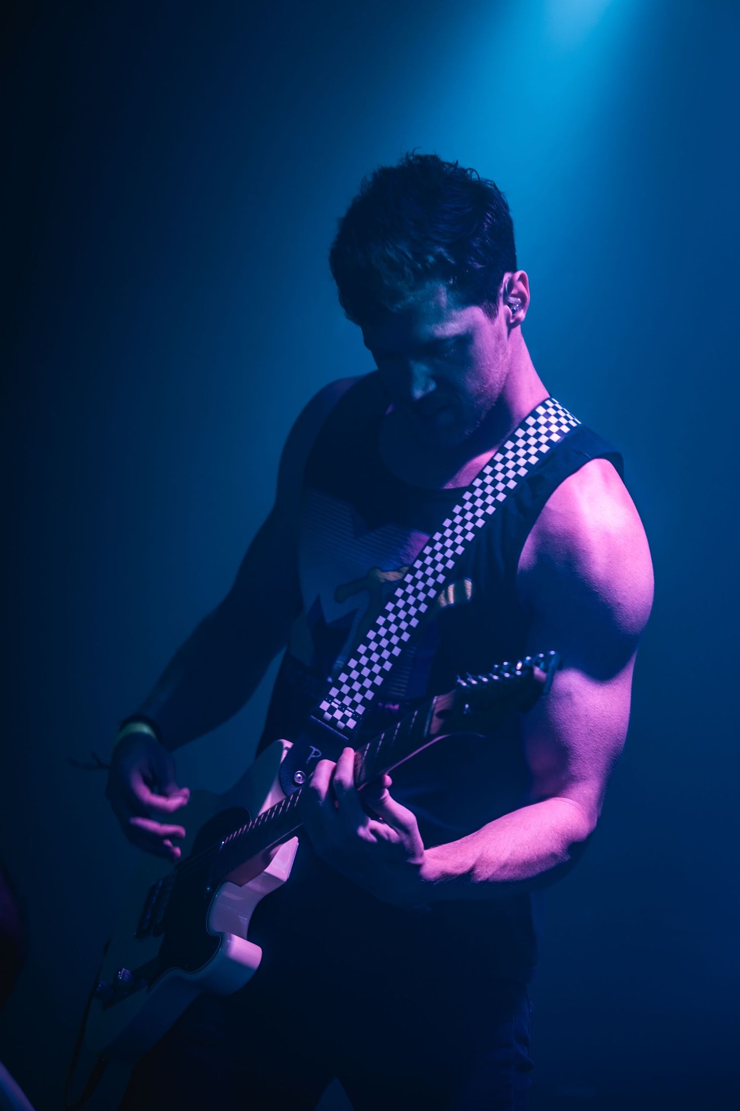 Guitarist performing on stage with checkered strap under dramatic blue lighting.