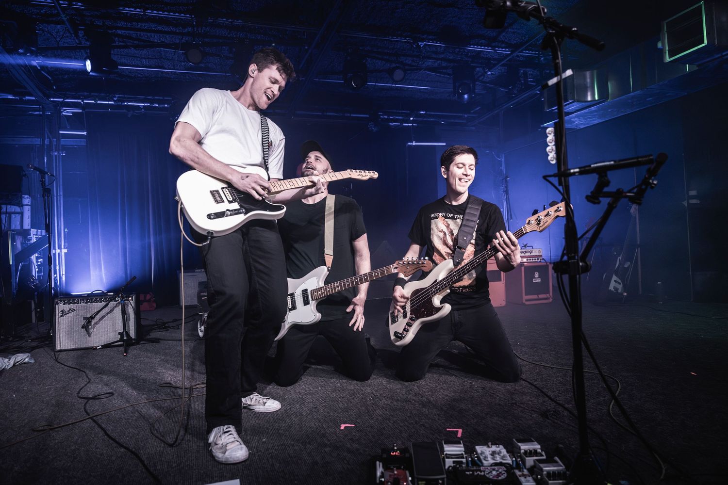 Musicians with electric guitars performing on dark stage with blue lighting.