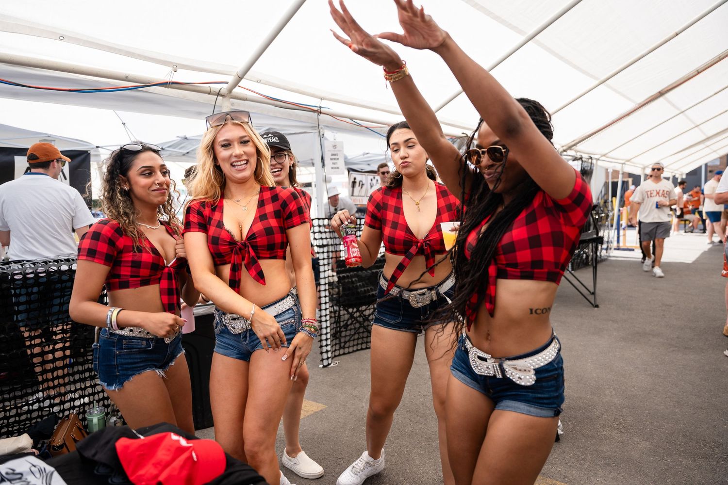Group of friends in coordinated red plaid tops dancing and celebrating at an outdoor festival.