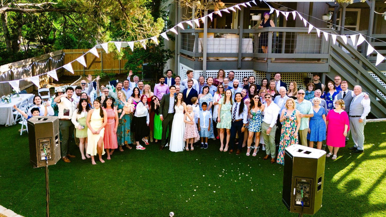 Large group photo of wedding guests gathered on a lawn with string lights and decorations.
