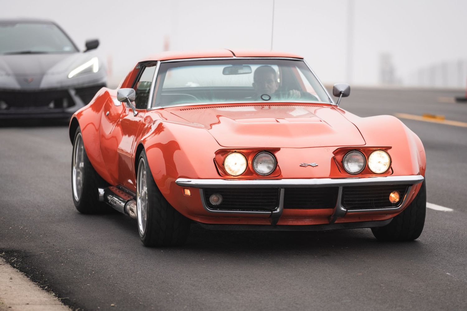 Classic orange Chevrolet Corvette Stingray with chrome bumpers in motion.
