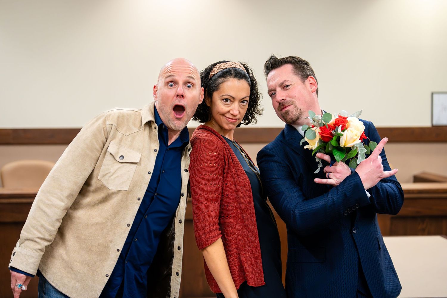 Three people pose playfully with flowers and dramatic expressions in a courthouse setting.