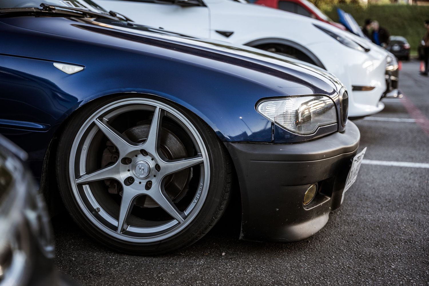 Close-up shot of a lowered sports car wheel with silver five-spoke rim against dark blue bodywork.