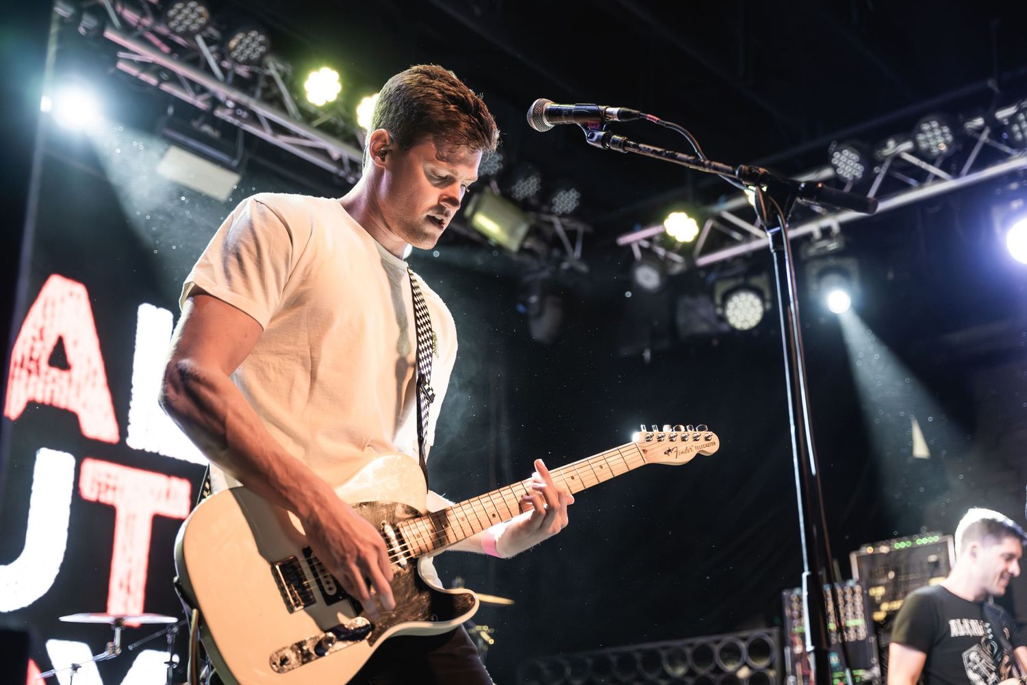 Guitarist performs under stage lights with dramatic side angle composition.