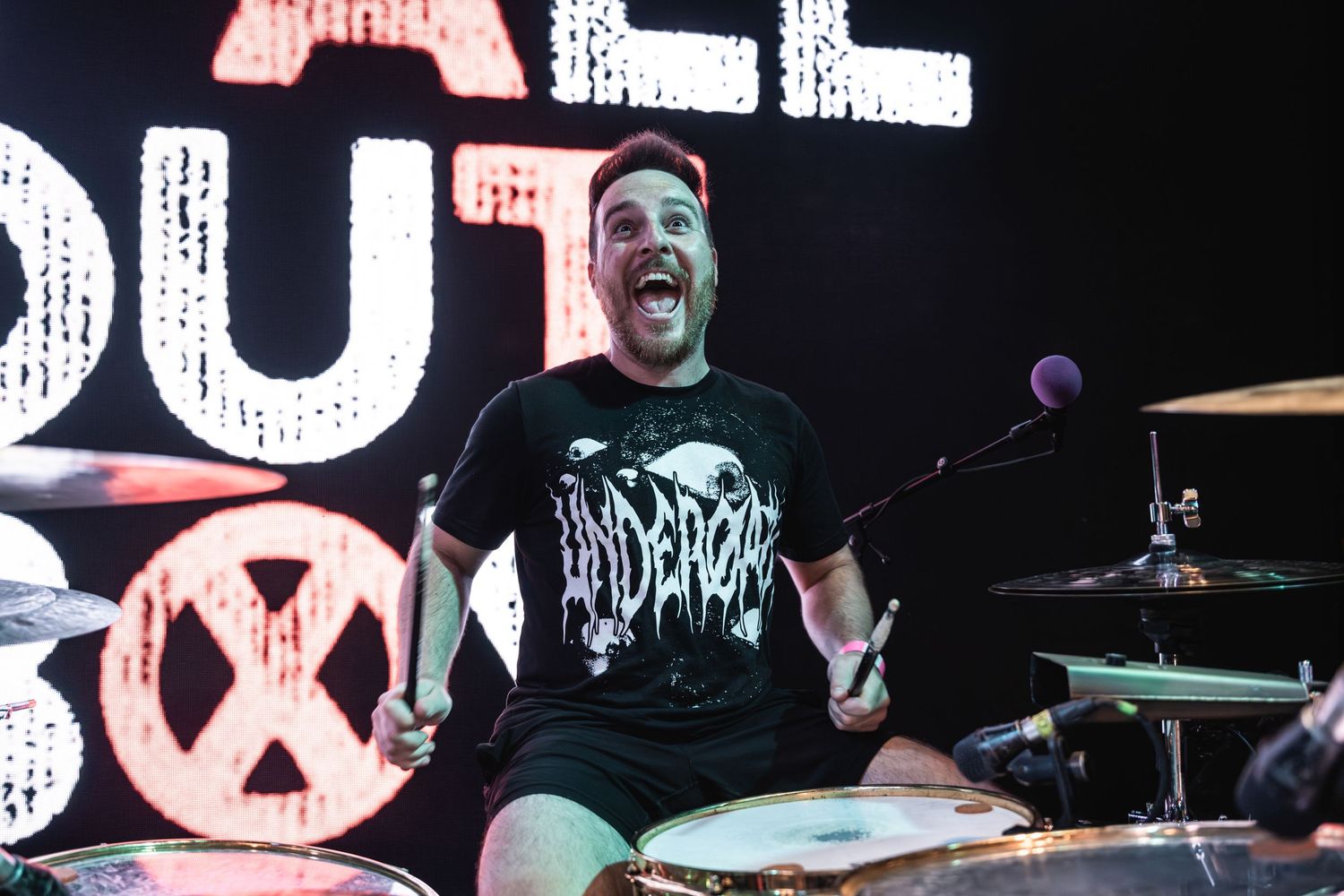 Animated drummer performing on stage with illuminated signage in background.