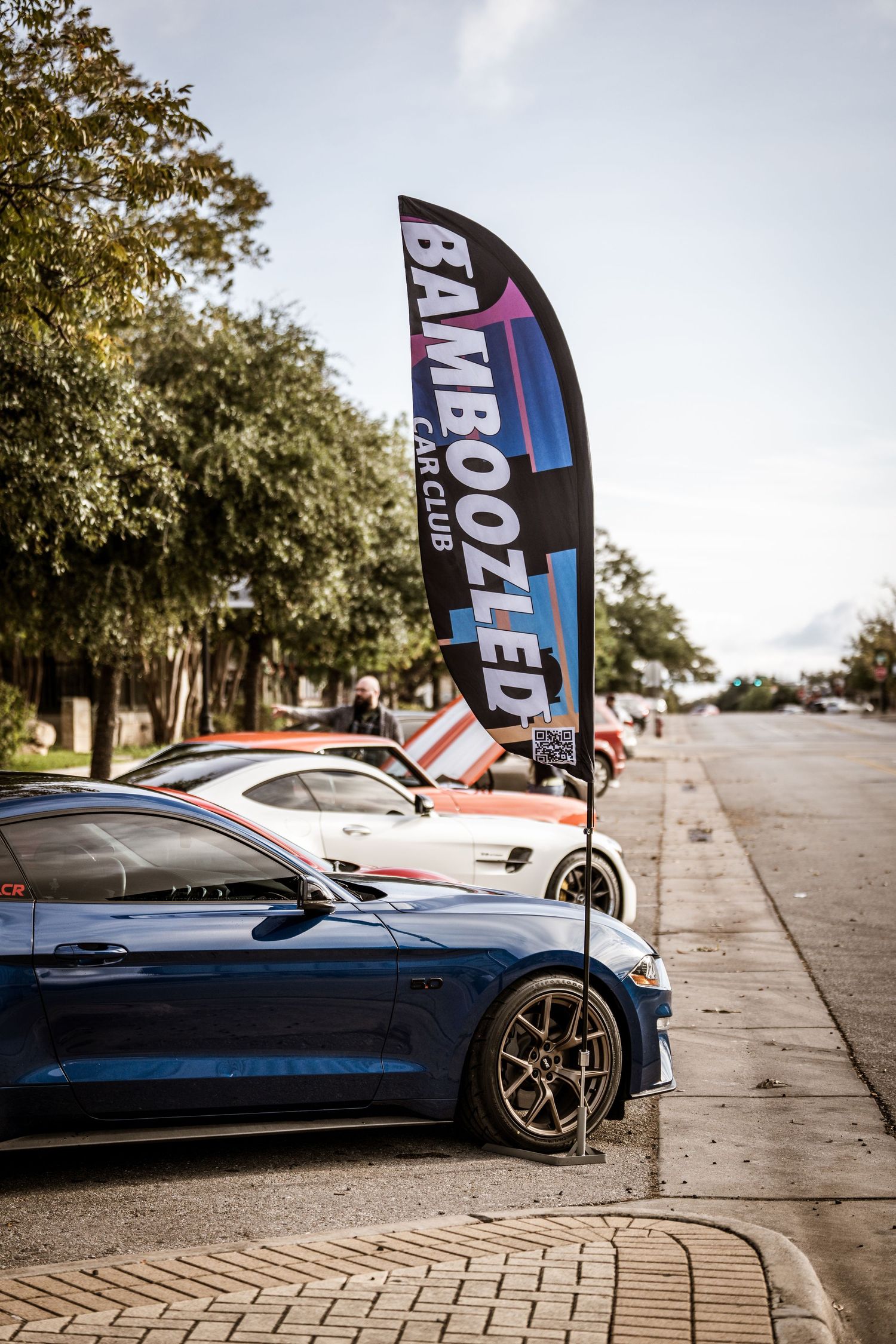 Blue sports car parked on a street with a Bamboozled event flag banner visible.
