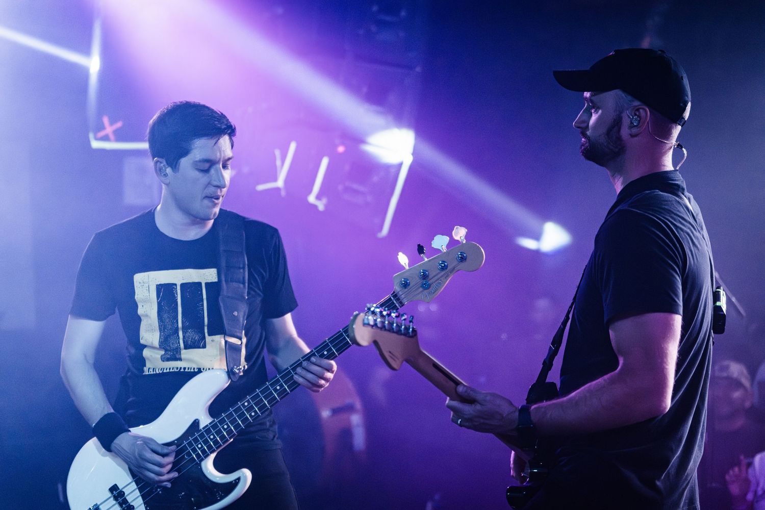 Two musicians playing guitars on stage with dramatic concert lighting.