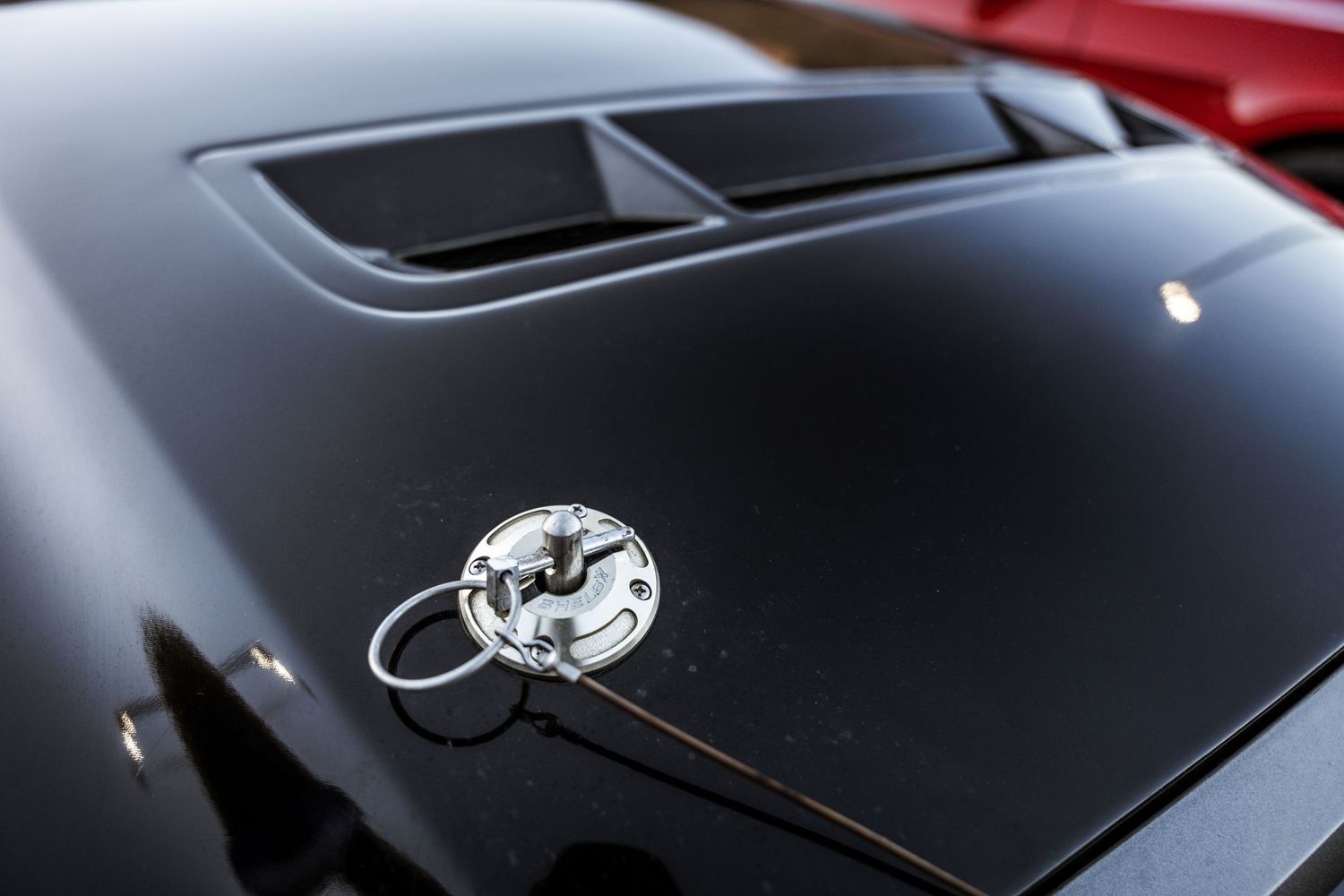 Close-up detail of a black car hood with decorative air vent and chrome emblem.