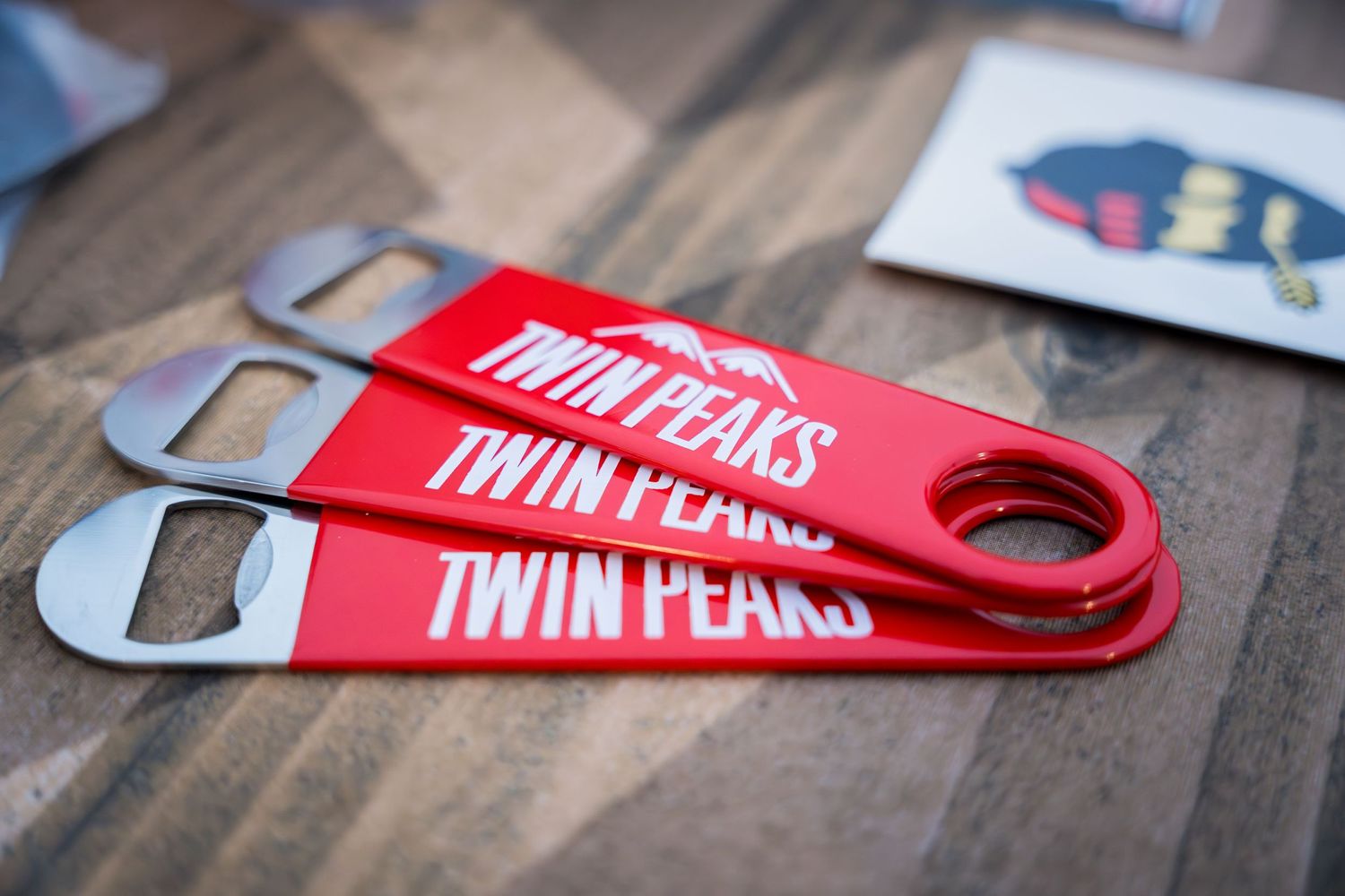 Three red bottle openers with Twin Peaks branding on wooden surface.
