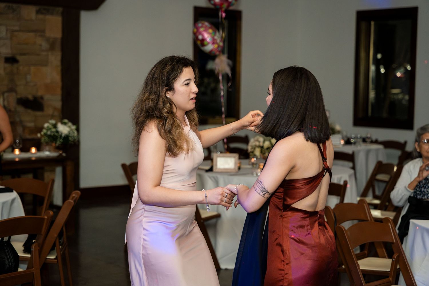 Two people dancing together at an indoor event venue with wooden chairs and brick walls in the background.