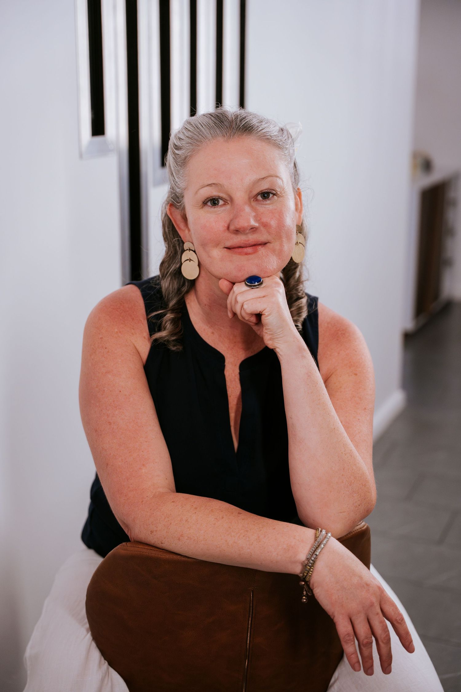 Portrait of someone sitting in a casual pose wearing a black sleeveless top and large earrings.
