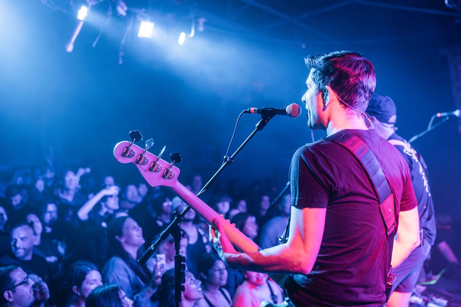 Concert performers on stage playing music in front of a crowd with dramatic blue lighting effects.