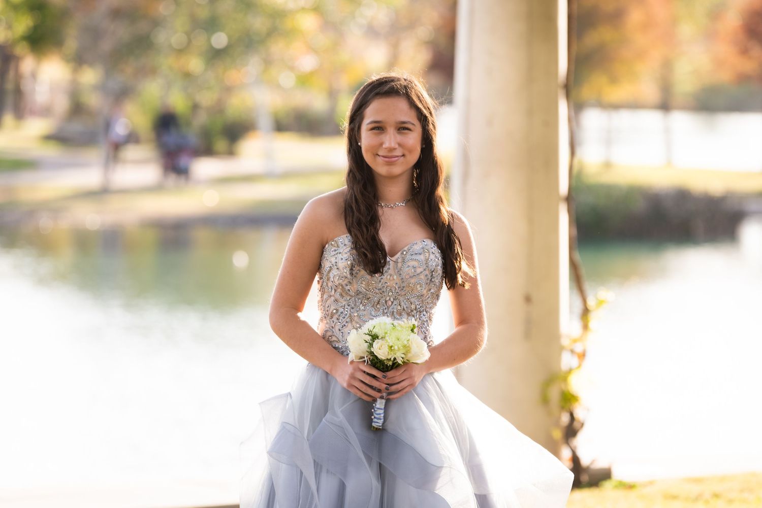 Elegant bridal portrait in a white gown by a lakeside with autumn trees.