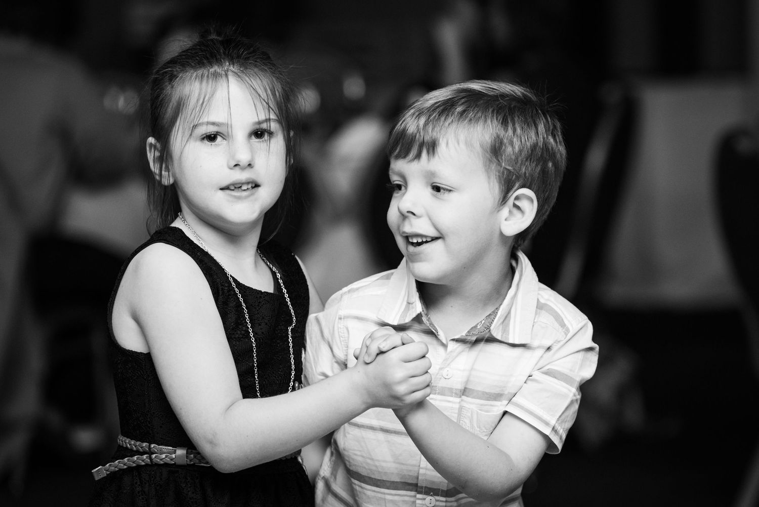 Two young children dancing together at a wedding reception in black and white.