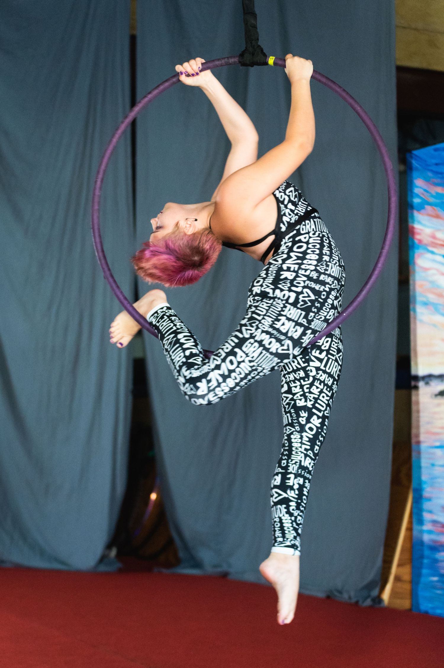 Dynamic aerial hoop performance featuring intricate backbend pose in black and white costume.