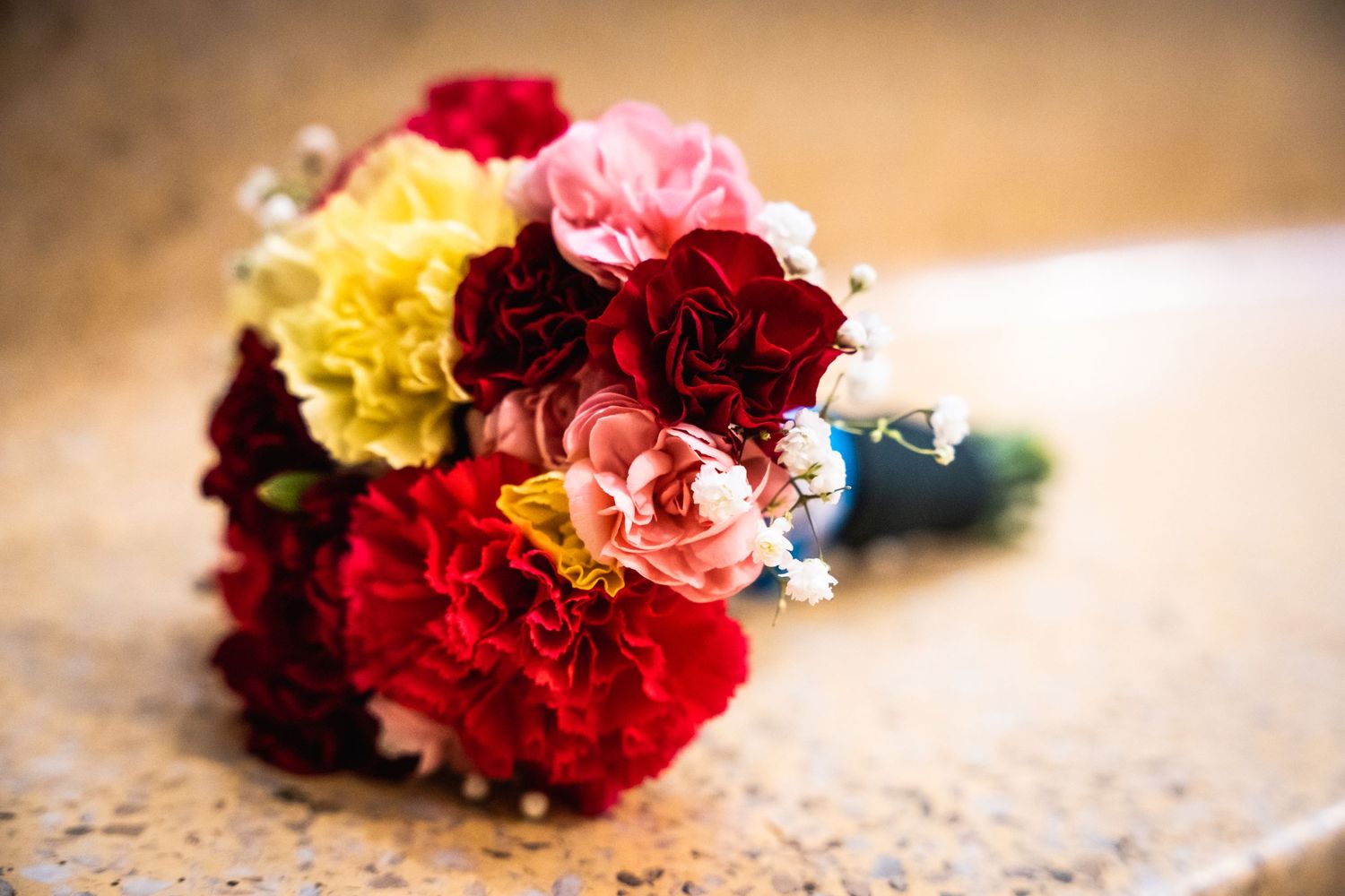 Vibrant bouquet of red, pink and yellow carnations with baby's breath against blurred background.