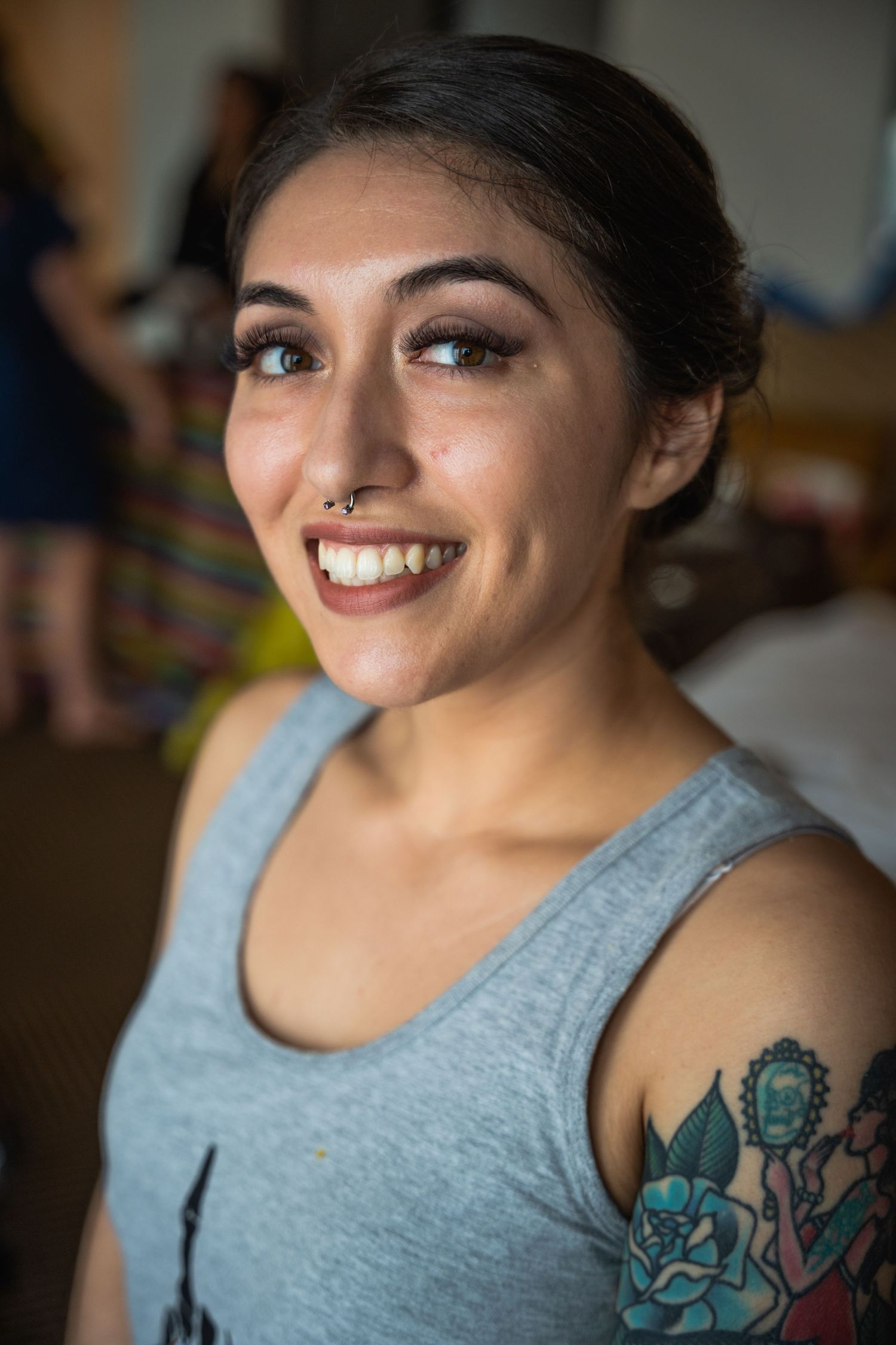 Close-up portrait showing bright smile and colorful arm tattoo while wearing a grey tank top.