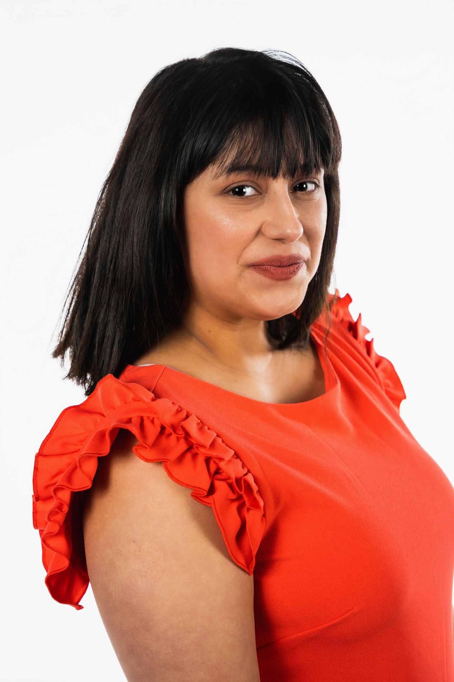 Portrait of woman in bright coral ruffled sleeve top against white background.