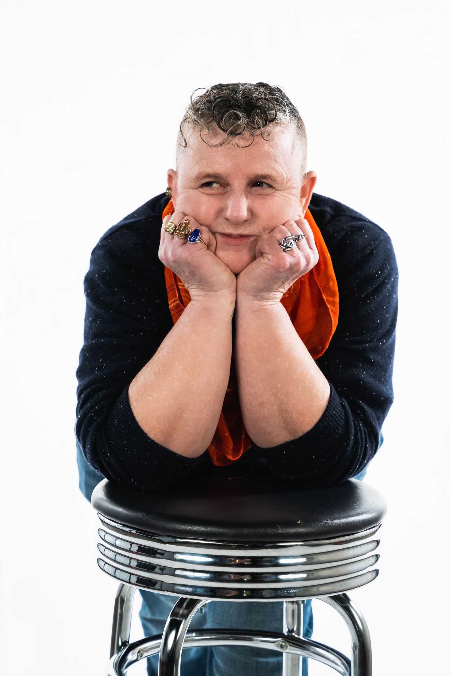 Someone poses playfully on a retro diner stool wearing a navy sweater and orange shirt.
