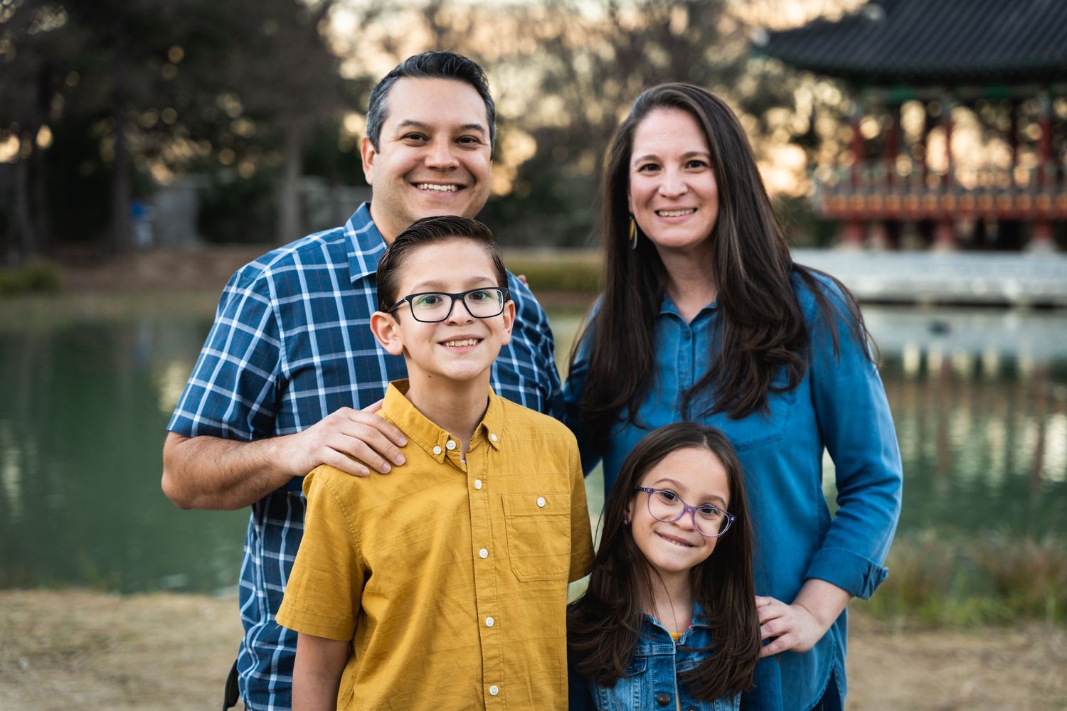 Small family group smiling together outdoors with lake in background at golden hour.