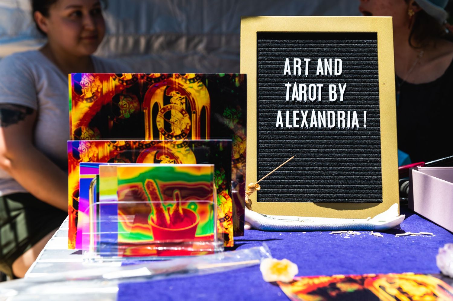 A letterboard sign advertising art and tarot readings next to colorful holographic displays.