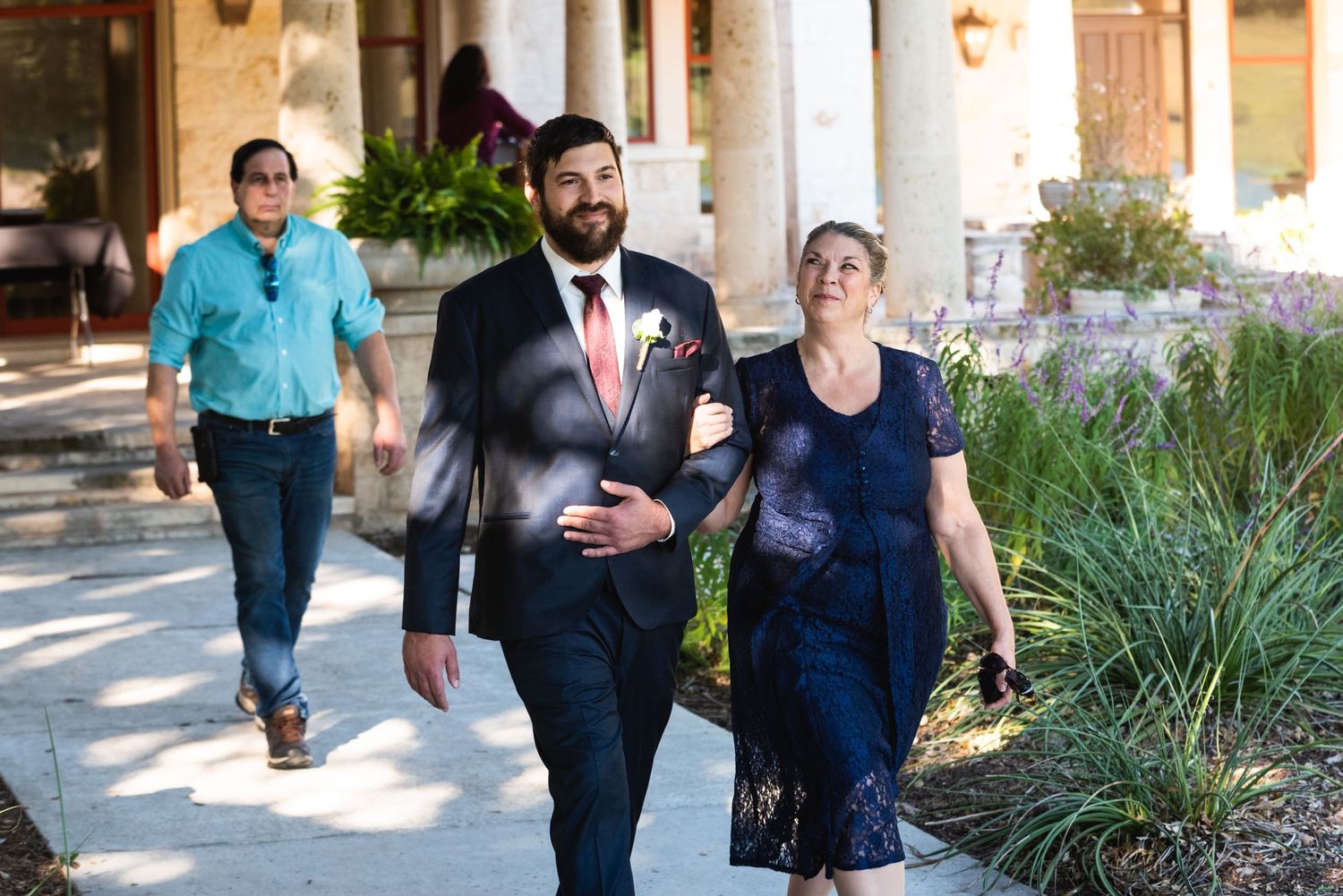 People walking along a stone colonnade pathway during an outdoor wedding ceremony.