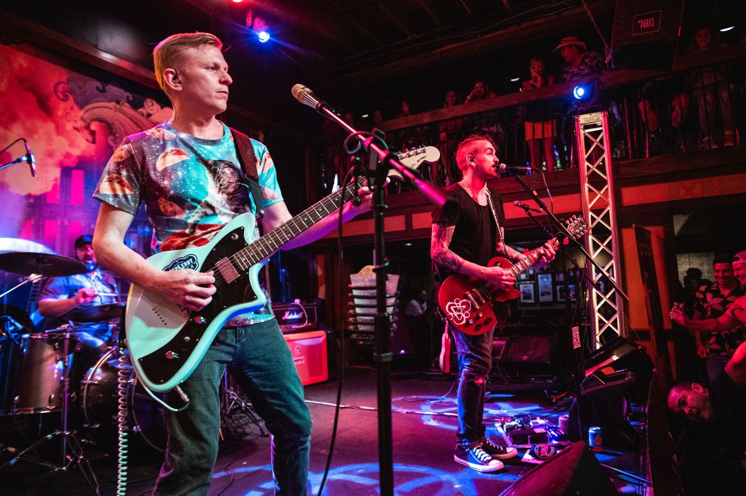 Musicians performing on stage with colorful lighting and equipment at a live concert venue.