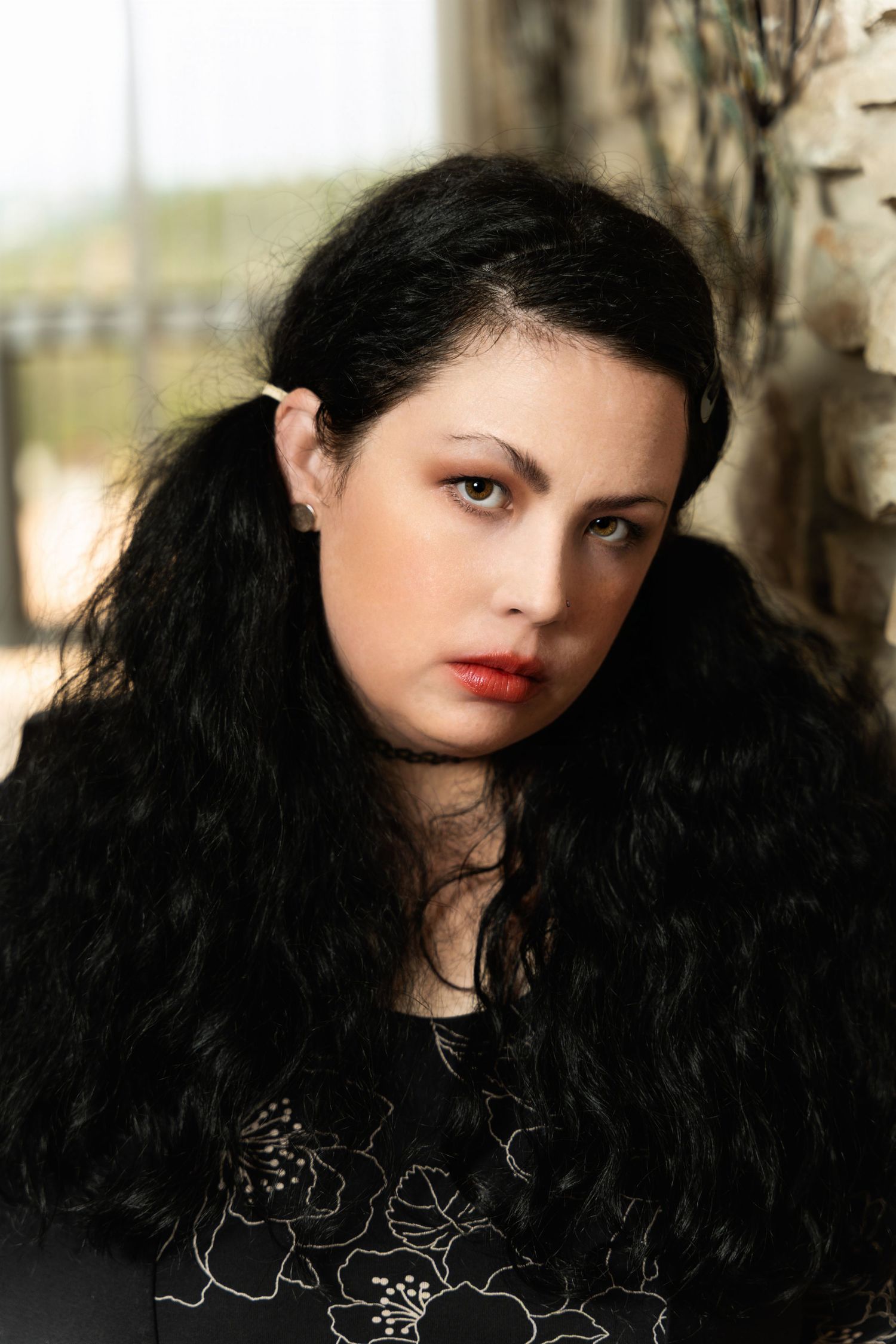 Dramatic close-up portrait with long dark hair against natural light background.