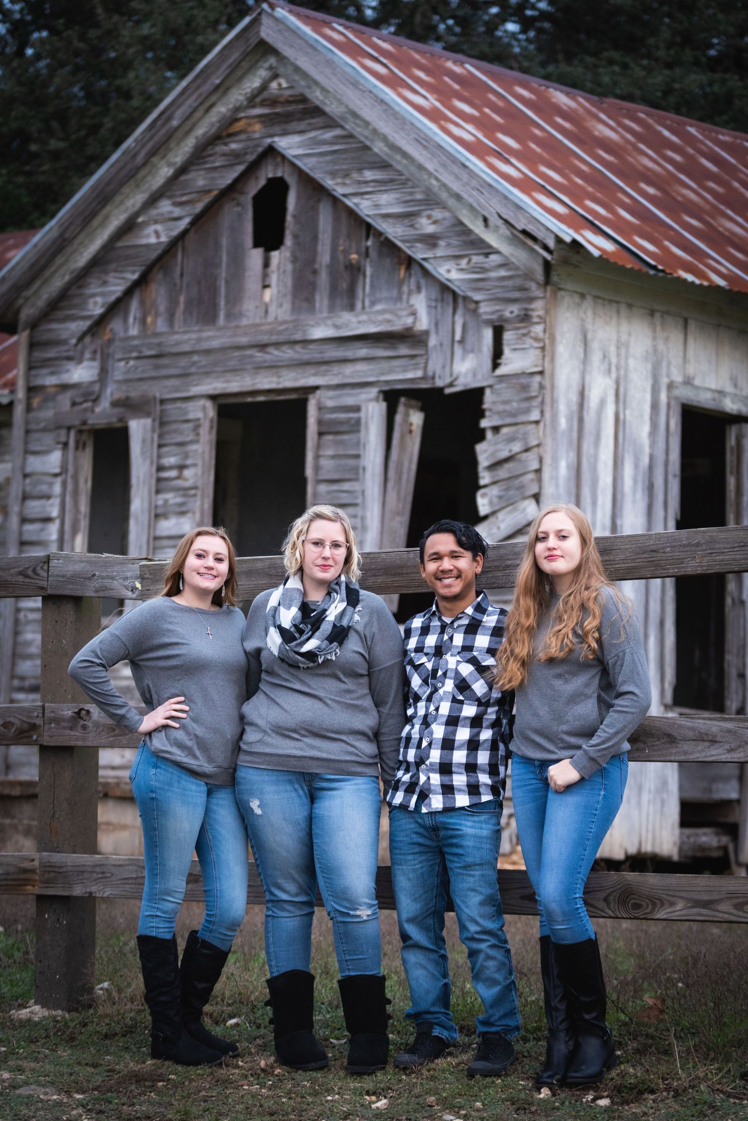 Four people pose together in casual outfits in front of rustic wooden building with metal roof.