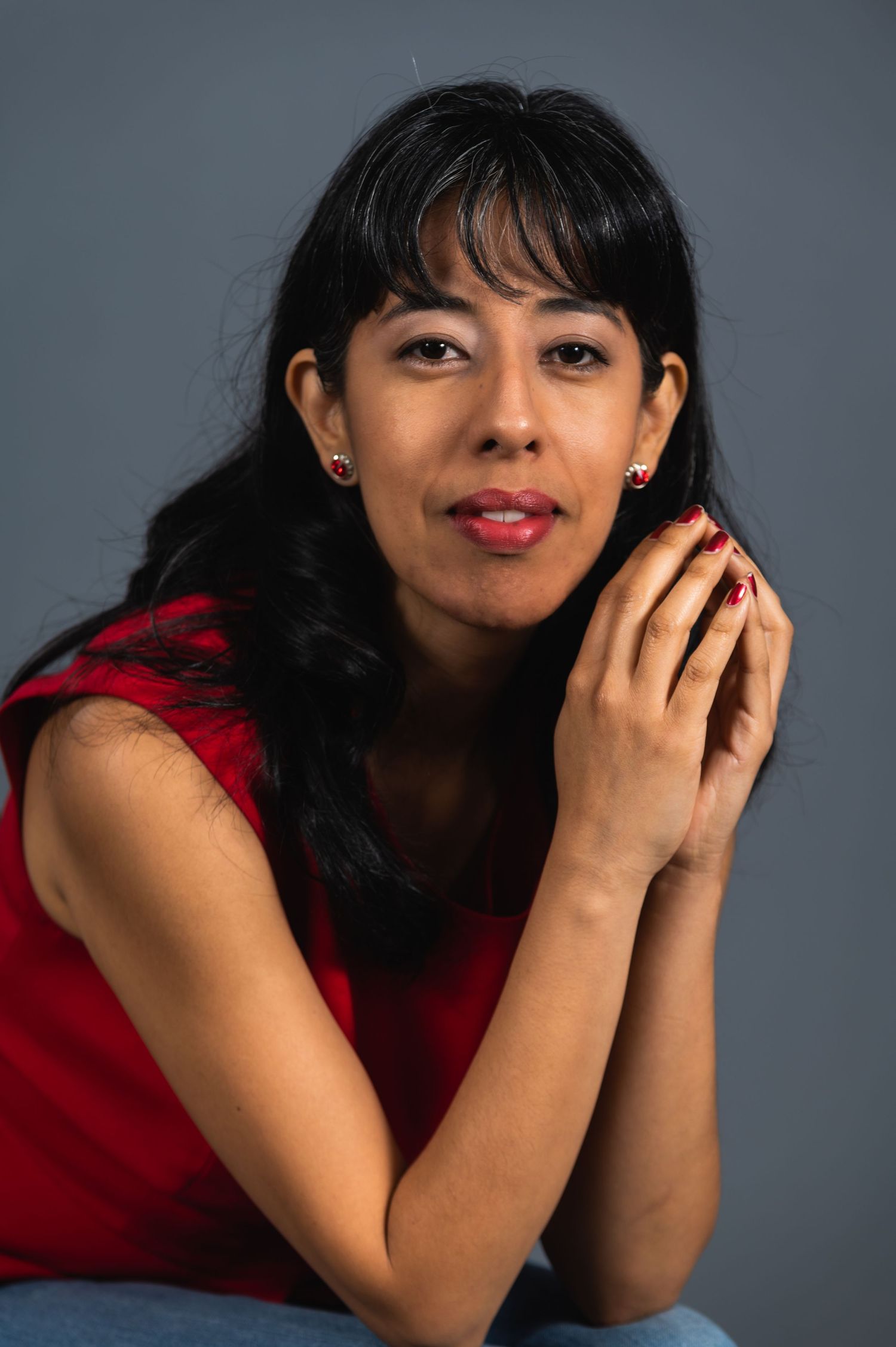 Studio portrait with dramatic lighting featuring woman in red top against grey background.