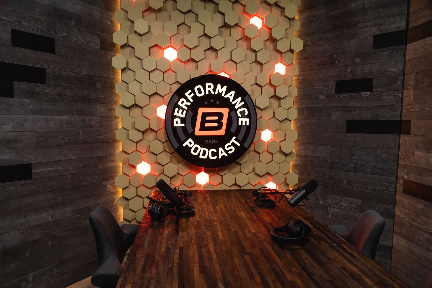 Empty podcast recording space with dark wood table and illuminated hexagonal backdrop.
