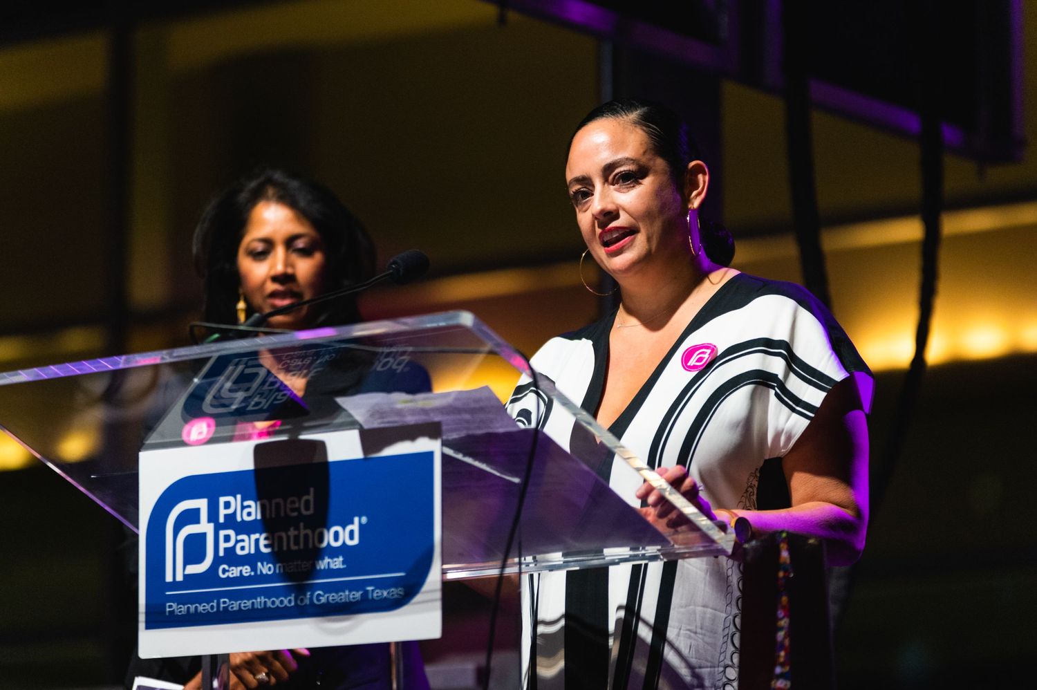 Two speakers present at Planned Parenthood podium during event with stage lighting.