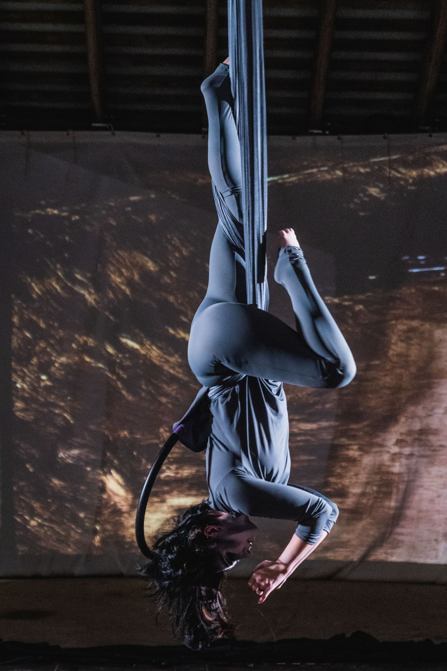 Aerial performer executing inverted pose on silk fabric against textured background.