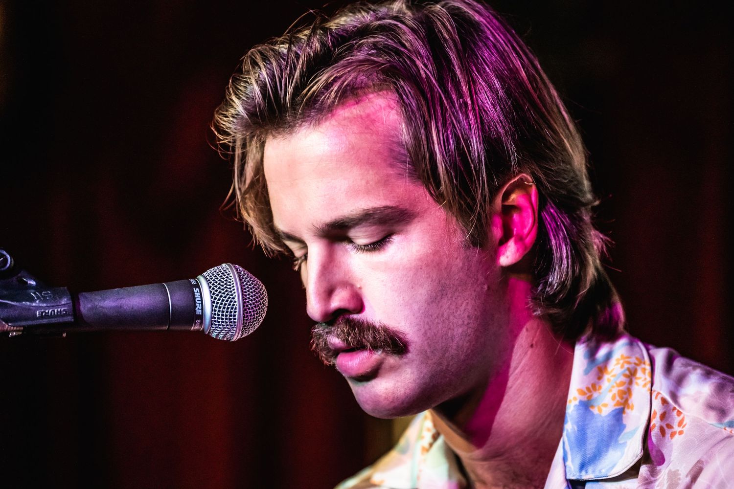 Musician performing on stage with microphone under dramatic purple lighting.