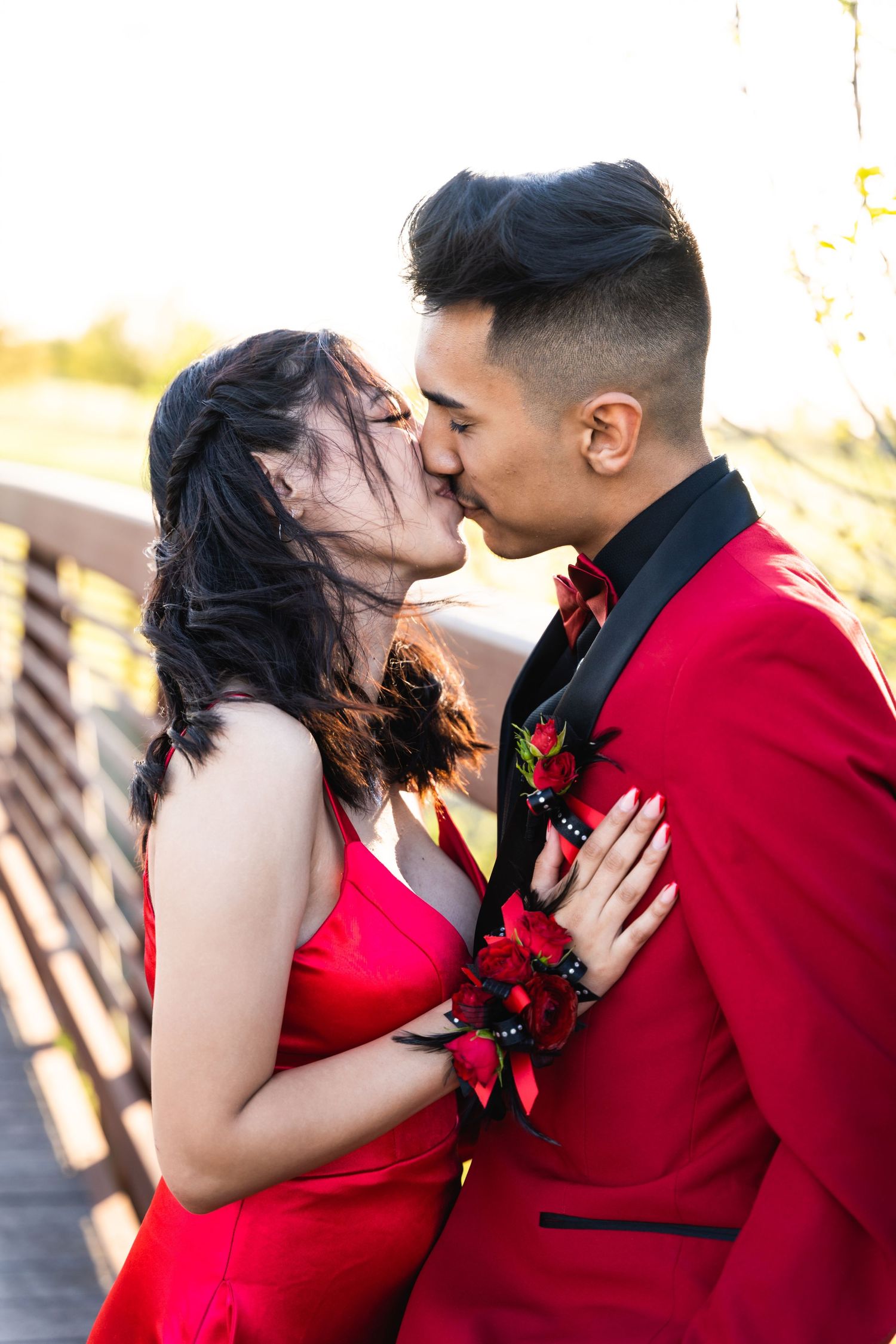 Romantic couple in red formal wear sharing an intimate moment on wooden bridge.