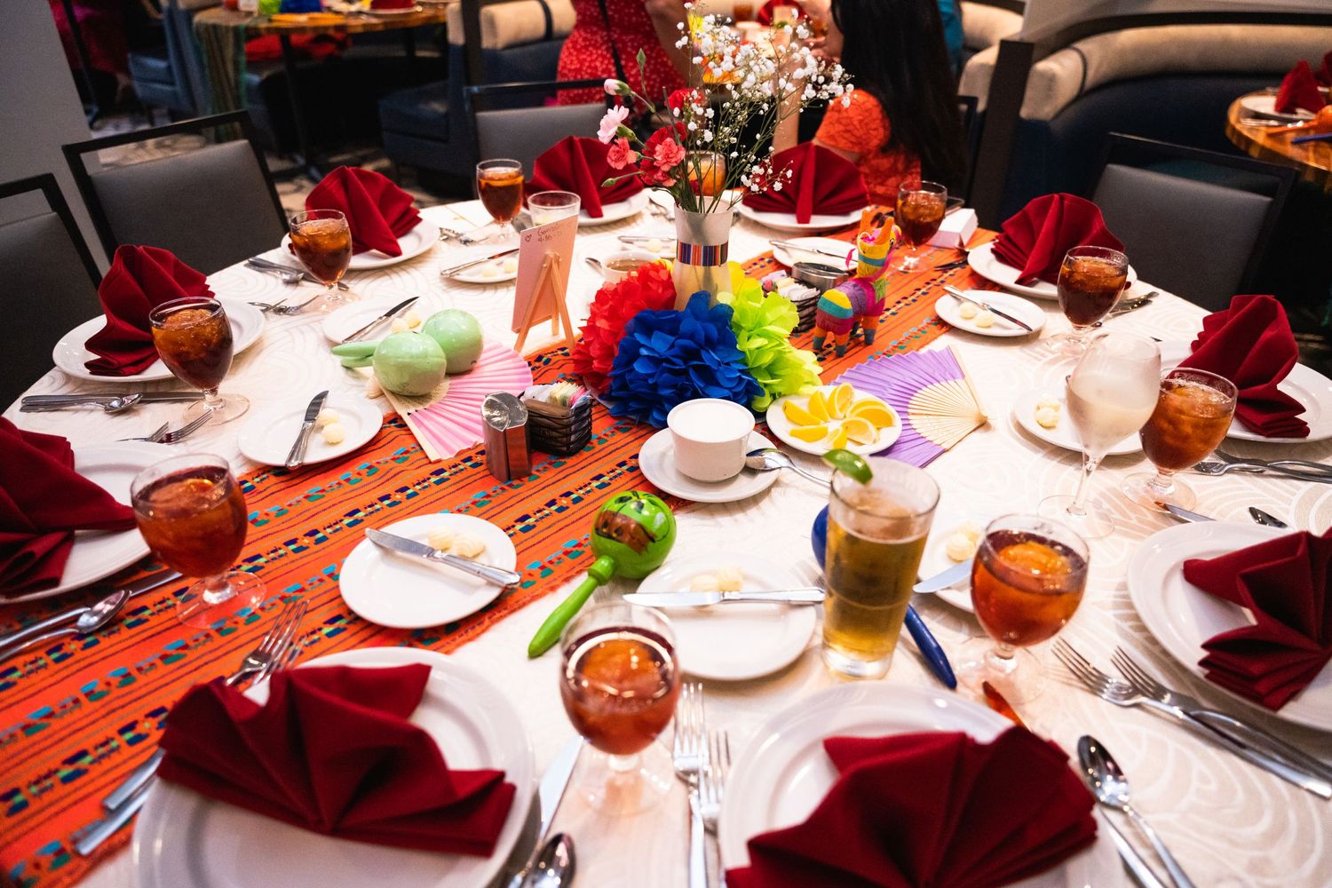A festively decorated wedding reception table with red linens and colorful floral centerpieces.