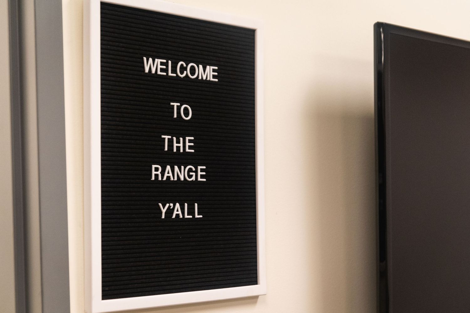 Black letterboard sign mounted on wall reading 'Welcome to the Range Y'all' in white letters.