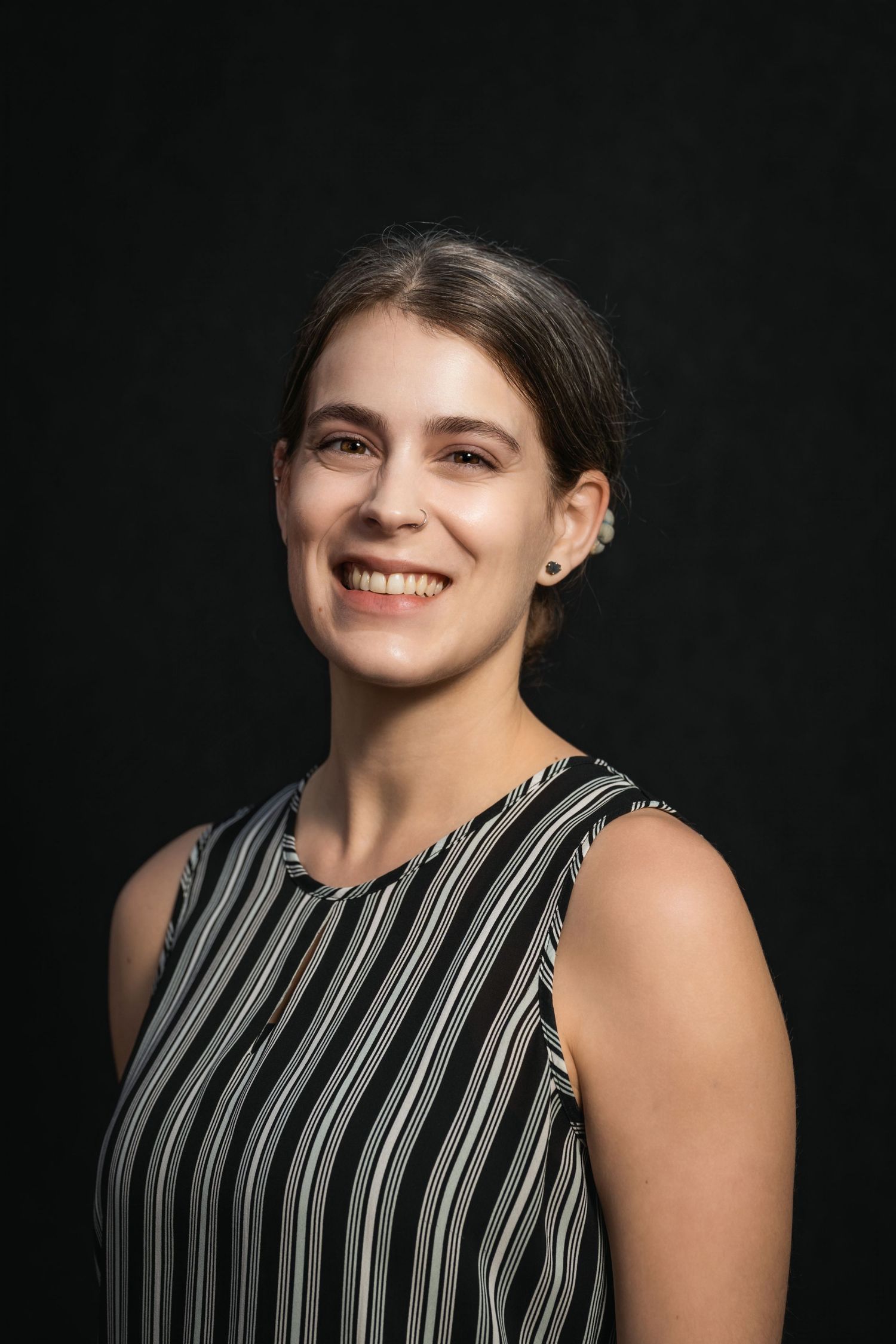 Studio portrait featuring person in black and white striped sleeveless top with natural smile.