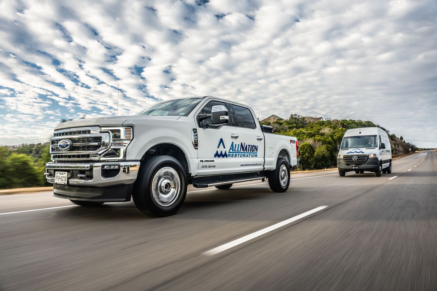 Two branded white Ford pickup trucks driving on highway with cloudy sky backdrop.
