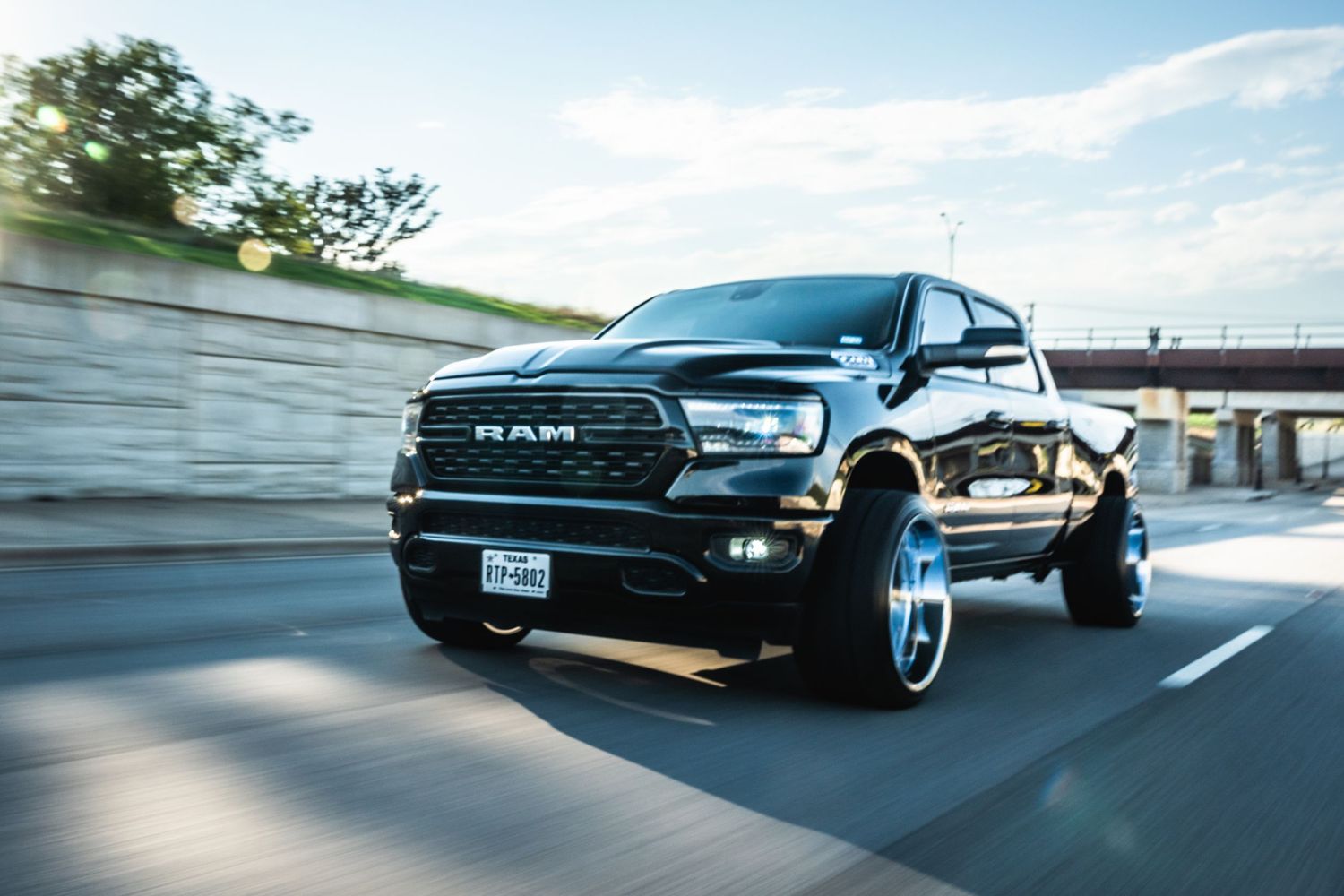 Black lifted RAM truck with custom chrome wheels driving on highway with motion blur effect.