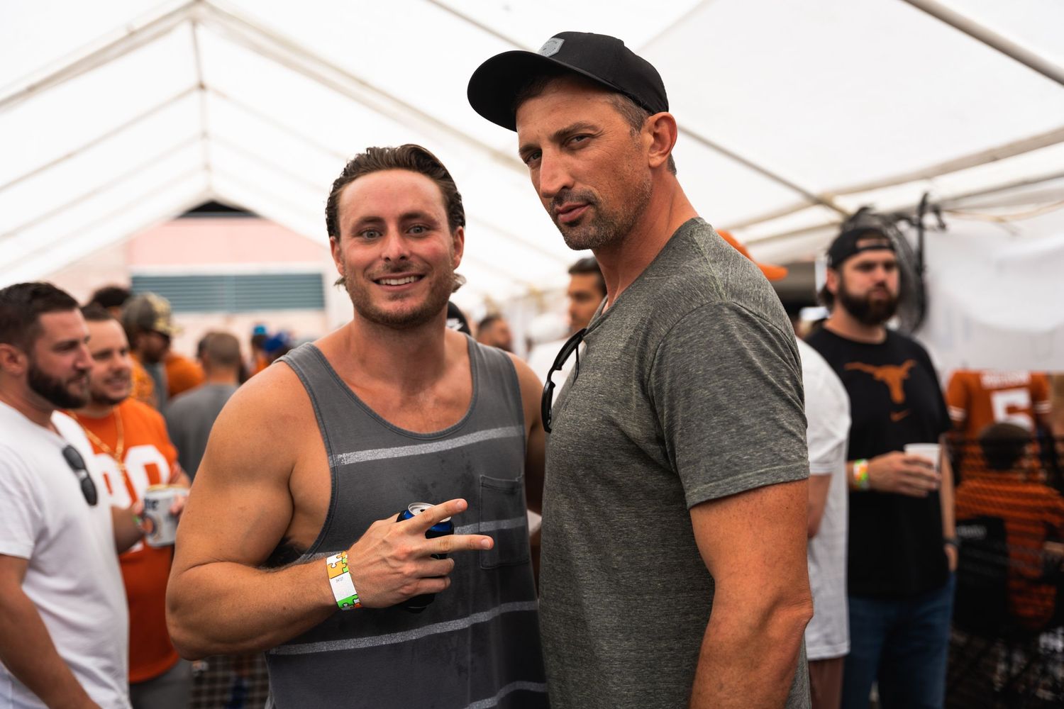 Two guests chatting while holding drinks at an outdoor party under a white tent.